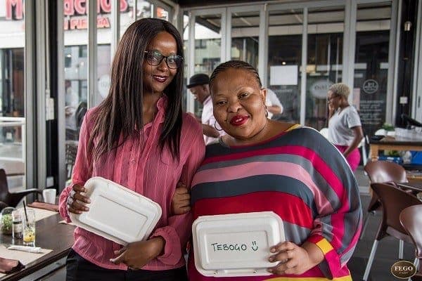 Two women holding GREEN HOME takeaway containers, smiling at the camera