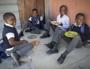 Four boys in uniform eating a meal outside