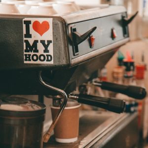 Close up of coffee machine with biodegradable coffee cup & 'I heart my hood' sticker