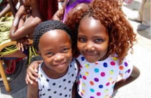 Two of the Yiza Ekhaya girls standing outside in the sun and smiling at the camera