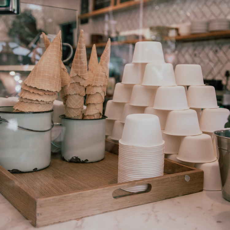 A stack of GREEN HOME bagasse bowls on a counter next to ice cream cones