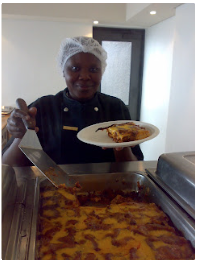 A restaurant worker smiling at camera holding a slice of lasagne on a Green Home bagasse plate