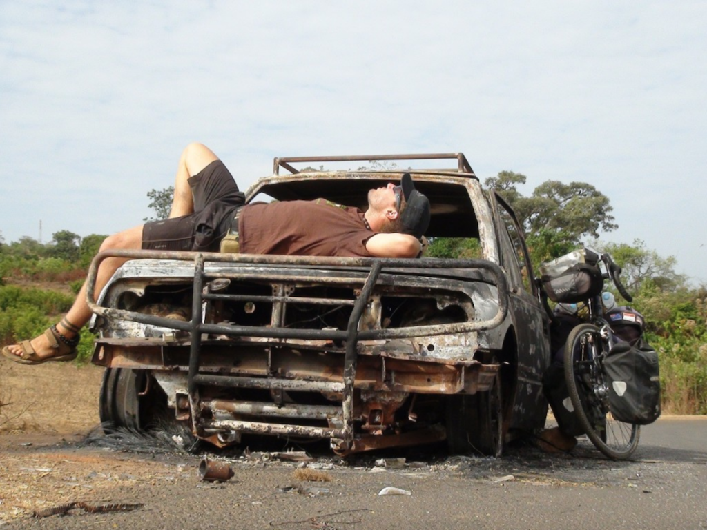 Kayden Kleinhans resting on the bonnet an old burnt out car with his bike leaning against the side
