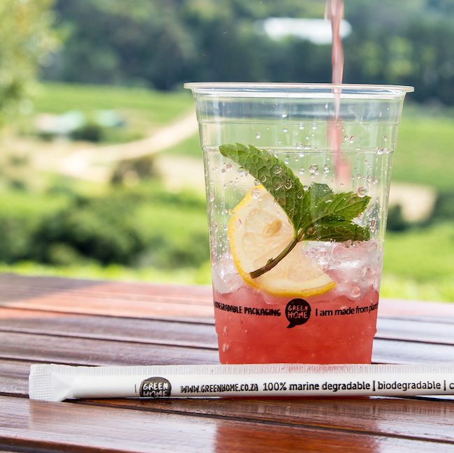 close up of a clear cup with ice, lemon and mint and red juice being poured into it. A paper straw lying in front.